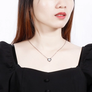 Gros plan d'un collier pendentif coeur minimaliste porté par un mannequin en haut noir