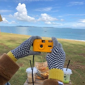 First-person view of black and white herringbone knit gloves with yellow cuffs by the sea