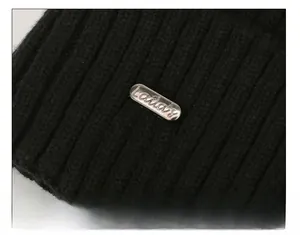Detail of black ribbed knit beanie featuring an oval silver metal logo plate on the side