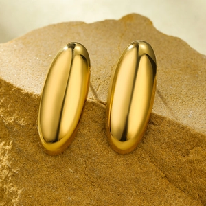 Detailed view of polished gold oval earrings resting on a natural stone background