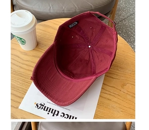 Detail view of burgundy cotton cap with interior stitching and adjustable strap on a table