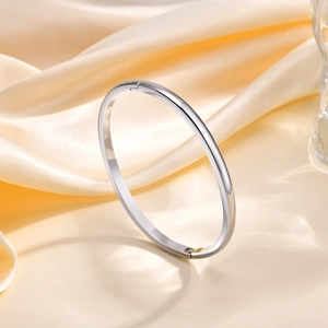 Polished stainless steel bangle with side opening clasp on soft gold silk fabric