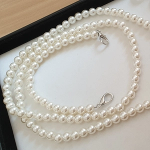 Macro detail of cream white pearl bag strap featuring silver metal lobster clasps on ends