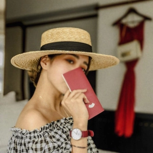 Detail of natural straw boater hat with a wide black ribbon worn by a model in a cozy room