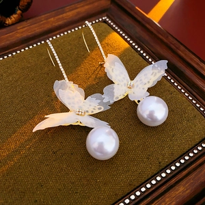 Detailed macro view of long pearl drop earrings with translucent mesh butterfly wings