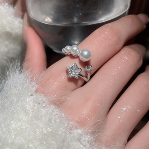 Close-up of zircon star and pearl open ring on finger with soft water shadows