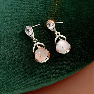 Macro shot of silver drop earrings with cat eye stones on dark green velvet surface
