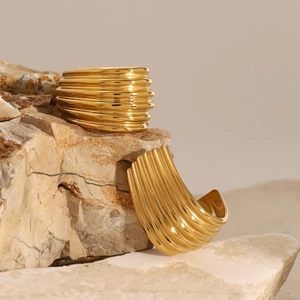 Polished gold multi-layered wavy earrings displayed on a natural brown stone texture