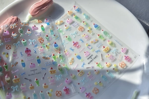 Détail d'autocollants pour ongles avec motifs de desserts et nœuds sur une assiette en céramique