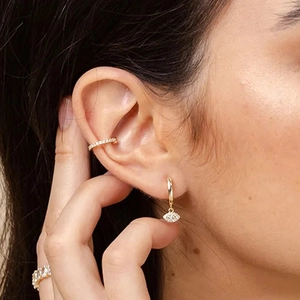 Detail view of gold huggie hoop with eye pendant, ear cuff, and cz ring on model