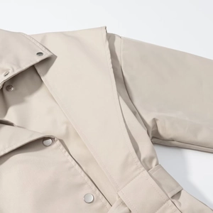 Detail of beige trench coat featuring silver metal snap buttons and premium double stitching