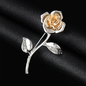 Macro detail of a two-tone rose brooch with golden flower and silver stem on black