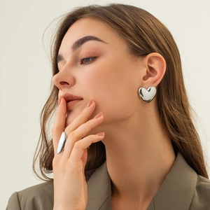 Minimalist silver heart earrings and oval ring set worn by model on beige backdrop