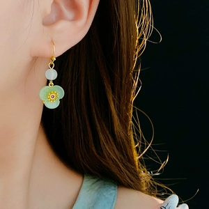 Macro shot of gold-plated flower earring with green jade-like petals on a model