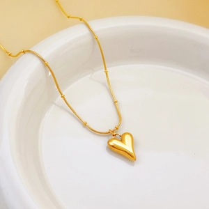 Minimalist gold titanium heart necklace displayed on a white ceramic plate