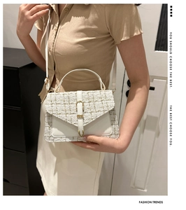Detail of white tweed shoulder bag with gold clasp and textured weaving pattern