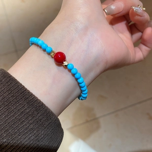 Gros plan du bracelet en perles turquoise avec perle rouge sur poignet féminin