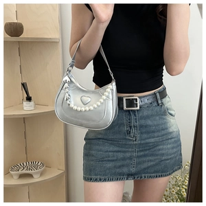Detail view of silver heart embossed handbag with faux pearl and metal heart chain strap