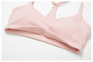 Detail of light pink sports bra with cross-back straps and reinforced elastic hem