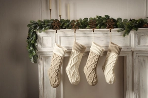 Set of four cable-knit Christmas stockings in beige and light brown hanging on a fireplace