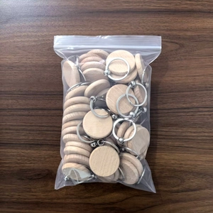 Bulk round beech wood keychains with metal rings in a clear bag on wooden desk