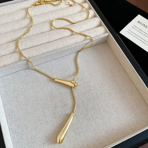 Detailed close-up of a glossy gold teardrop pendant on a sleek snake chain necklace