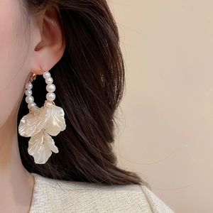 Close-up of elegant floral pearl earring on a model featuring white petals and gold details
