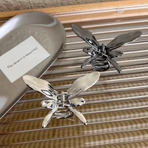Metallic butterfly hair claws in silver and dark grey on a textured glass surface