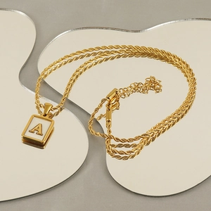 Detail of gold square pendant with white shell inlay and letter A on twisted chain