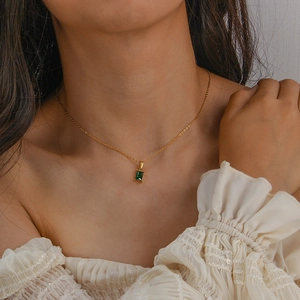 Gros plan d'un collier doré avec un pendentif en zircon vert carré sur un modèle