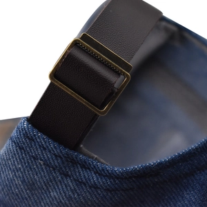 Détail de la sangle en cuir marron et de la boucle en bronze sur la casquette en denim