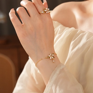 Dettaglio di bracciale e anello placcati in oro con fiori in smalto bianco e zirconi