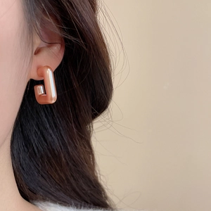 Close-up of a pink-orange geometric rectangular earring with a pearlescent finish