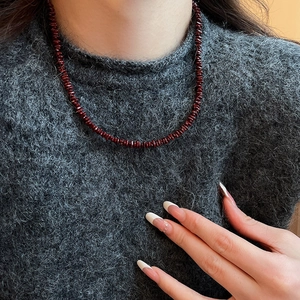 Macro shot of dark red beaded necklace beads against a grey knitted sweater background