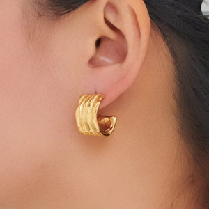 Close-up of golden C-shaped earring with hammered texture and polished metal finish