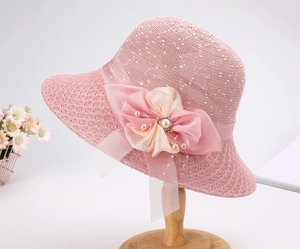 Dettaglio di cappello di paglia rosa con fiore in chiffon, centro perla e nappe