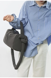 Detail of a charcoal gray puffy cylinder bag with knot strap on a striped shirt