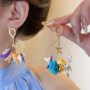 Close-up of golden hoop earrings with colorful shell pendants and small star charms