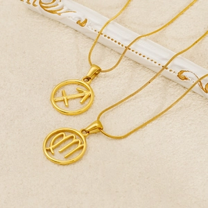 Detail showing two gold zodiac pendant necklaces on a textured surface with decor