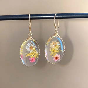 Primer plano detallado de pendientes ovalados de resina con flores reales secas.