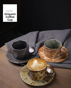 Close-up of three origami style ceramic coffee cups with saucers on a dark wooden table