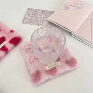 Pink plush heart coaster with soft faux fur texture under a glass in a cozy setting
