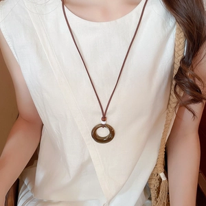 Close-up of a round amber resin pendant necklace with long cord on a white linen shirt
