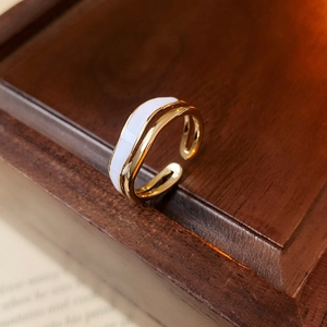 Close-up of gold double-layer wave ring with white enamel finish on a wooden box