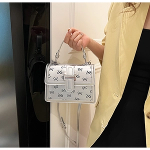 Borsa quadrata argento con fiocchi neri tenuta da una modella con giacca gialla