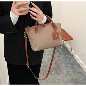 Chic khaki nylon tote bag with brown leather handles worn by a model in a black suit