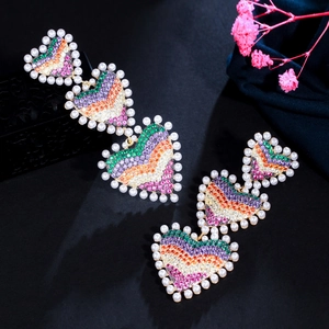Gros plan de boucles d'oreilles en cœur avec strass colorés et perles blanches sur noir