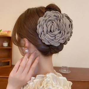 Detailed view of a grey fabric flower hair claw clip on a woman's hair bun