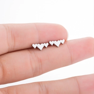 Close-up showing a pair of polished silver heart-shaped stud earrings held in hand