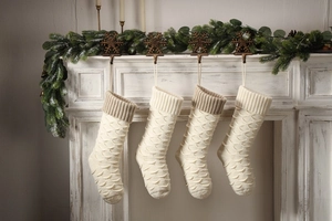 Detailed view of four large knitted Christmas stockings with fish scale textures on a fireplace